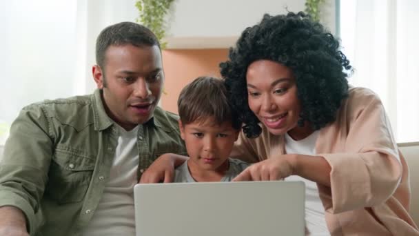 多种族家庭快乐的妈妈爸爸儿子一起看笔记本电脑非裔美国人父母妈妈爸爸和收养的白人小男孩孩子赢得了成功喜庆胜利情绪在家里感到惊奇 — 图库视频影像