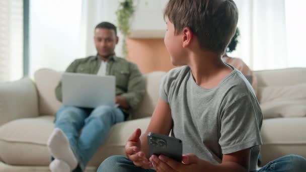 家有多种族父母用笔记本电脑吸毒成瘾的家庭忽视悲伤的孩子小男孩无聊的孩子在地板上拿着手机智能手机缺乏父母的注意监护 — 图库视频影像