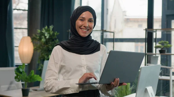 Islam businesswoman in hijab Arabian Indian muslim islamic woman business entrepreneur manager girl with laptop commerce working studying online browsing computer smiling toothy at camera in office