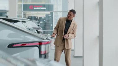Neşeli müşteri Afro-Amerikalı müşteri müşteri balosu otomobil galerisinde yeni lüks elektrikli araba satın alımını kutluyor. Milenyum dansı yapan mutlu duygular dans eden iş adamı galeride kiralık araba satın alıyor.