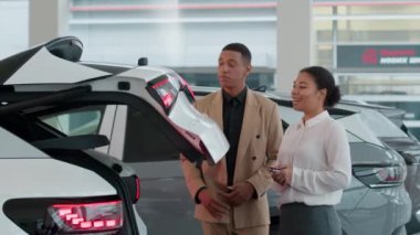 Otomobil satıcısı kadın, otomobil çapraz özelliklerini inceleyen afro-amerikan erkek alıcı müşteri galerisindeki yeni modern elektrikli ulaşım aracını otomatik olarak tanıttı.