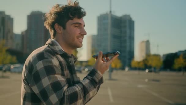 ハッピーコーカサス人の男は スマートフォンのウォーキングシティストリートで音声メッセージを記録します 笑顔の男 携帯電話の友人とチャット オンラインメッセンジャーレコード スピーカーフォンのスピーカーと音声ボイスメール — ストック動画