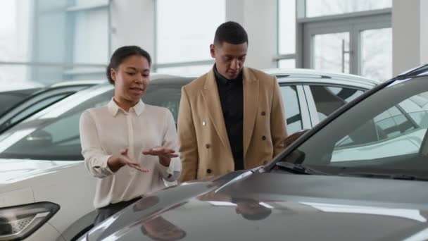 非洲裔美国人夫妇在汽车展示厅购买新车女销售员经销商女销售员向男性客户咨询选择豪华汽车的交叉经销商商业交易 — 图库视频影像