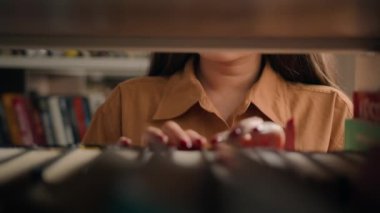 Yakın plan tanınmayan kadın öğretmen kız öğrenci, kitap kurdu, kütüphane rafında okumak için gerekli kitapları araştırıyor ve edebiyat kitaplarında ders kitabı arıyor.