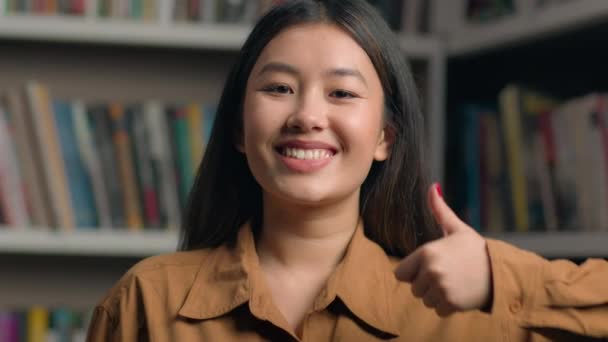 초상화 아시아 도서관에서 카메라를 제스처 엄지손가락을 보여주는 성공적인 피드백 — 비디오
