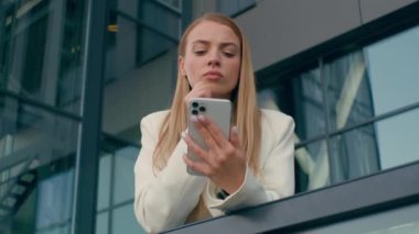Dalgın başarılı Kafkas kadın iş kadını profesyonel düşünceli iş kadını ofis yöneticisi açık hava kurumsal binasında akıllı telefon düşünen, telefonla medyayı karıştıran
