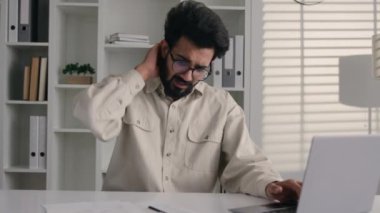 Arap Hintli iş adamı, ofis masasında dizüstü bilgisayarda çalışan erkek, boyun ağrısı, sırt ağrısı, bilgisayar, sağlıksız hasta iş adamı masajı, omurga kasları, sağlık hizmetleri.
