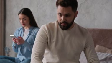 Kafkasyalı çift sorunlu ilişki üzgün adam yatakta karısından ayrı oturuyor bağımlı alet bağımlısı cep telefonlu akıllı telefon koca internet sosyal medya bağımlılığını görmezden geliyor