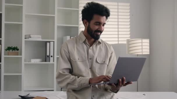 阿拉伯办公室职员30多岁留着胡子的男性程序员站在工作场所公司微笑着商人工作笔记本电脑在线打字与客户聊天阿拉伯商人在镜头前积极笑 — 图库视频影像