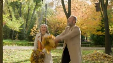 Emekli çift, çılgın, mutlu erkek, dışarıda birlikte eğleniyor. İki büyük anne ve büyük baba, yaşlı eş, koca, kadın, sonbahar parkında sarı yapraklar fırlatıp sonbahar doğası şehrinin tadını çıkarıyor.