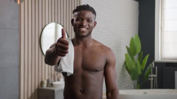 快乐的非裔美国人 光着身子笑着 英俊的30多岁的男人 拿着浴巾 看着相机 露出大拇指的姿势 在家庭护理美容美发广告上 早上好 浴室淋浴 — 图库视频影像