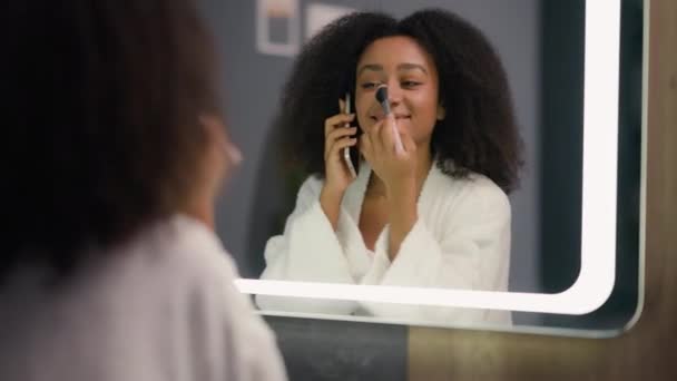 女性の鏡の反射幸せな女の子話す携帯電話の通話の美しさの訪問は化粧品の話のスマートフォンを準備する顔の調子のための粉を適用します — ストック動画