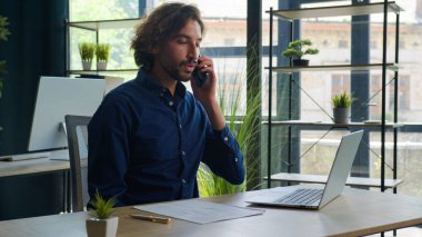 Ortadoğu Arap iş adamı cep telefonundan konuşur ofis girişimcisinin bilgisayarında çalışan yasal kontratı kontrol eder müşteri uzak iş iletişimi erkek cevap teknolojisi kullanıma danışır