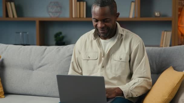 アフリカ系アメリカ人男性男性クライアント顧客ビジネスマンフリーランサー 自宅のソファでラップトップを入力 インターネットでのオンラインストア予約 リモート送信メールブラウジングメディアネットワーク — ストック動画