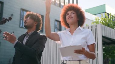 İki farklı etnik çeşitlilikte iş adamı şehirde geziniyor. Gayrimenkul projesini tartışıyorlar. Afrikalı Amerikalı kadın, ticari gökdelenleri Hintli Arap adamla konuşurken gösteriyor.