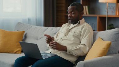 Sinirli, hoşnutsuz, stresli, Afrikalı, Amerikalı erkek, müşteri müşterisi, iş adamı, internetteki konferansta tartışırken evinde dizüstü bilgisayarla video üzerinden kızgın bir şekilde konuşan işadamı.