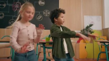 Mutlu şirin Afrikalı ve Kafkasyalı küçük okul çocukları çok ırklı kız ve erkek çoklu etnik çeşitlilikteki çocuklar okul çocukları sınıfta birlikte eğleniyorlar müzik dansı eşliğinde eğlenceli dans ediyorlar.