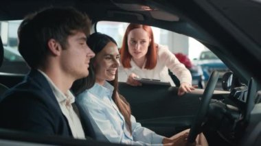 Yeni arabada oturan mutlu karı koca, beyaz kadın satış elemanı lüks araba seçiyor. Müşterilere, aile çiftlerinin araba satın almalarına yardımcı oluyor.