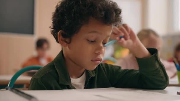聪明的非洲裔美国男孩认为写笔记是一项任务上体育课学校学抄本的男孩男孩男孩认为学习小学教育是在课桌前进行的 — 图库视频影像