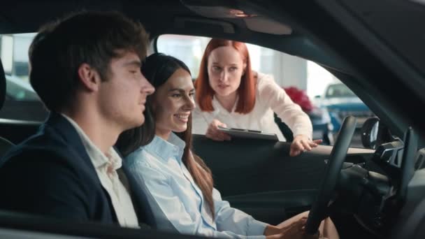新車の中に座っている幸せな夫と妻は豪華な自動車を選択します 白人女性 セールスマン ディーラー ヘルプ クライアント バイヤー カップル ディーラーの購入 レンタカー — ストック動画