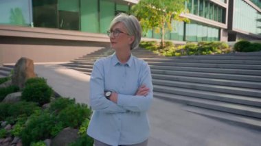 Açık hava portre işi girişimcisi yetişkin 50 'li yaşlarda kadın Kafkas iş kadını olgun orta yaşlı, yaşlı, beyaz saçlı, kendine güvenen kadın şehirde kameraya bakan başarılı bir çapraz el kamerası.