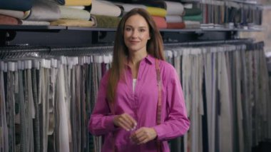 Kafkas kadın moda tasarımcısı terzi terzisi kameraya bakıp gülümseyen kadın satış elemanı kumaş mağazasında atölye dikme terzisi el işi konseptine bakıyor.
