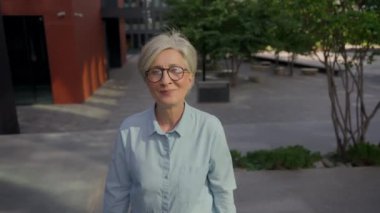Gülümseyen yetişkin beyaz iş kadını olgun orta yaşlı, beyaz saçlı iş kadını mutlu 50 'li yaşlarda kadın açık havada merdivenlerden çıkıyor kendine güvenerek yukarı doğru yürüyor kariyer hayalleri kuruyor.