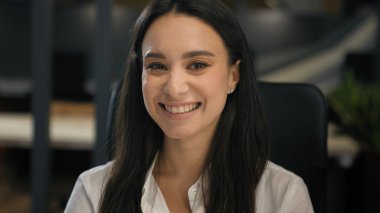 Beyaz iş kadını ofiste çalışıyor. Şirketin iş yerinde gülümseyen kameraya bakıyor. Şirket çalışanlarına gülümsüyor.