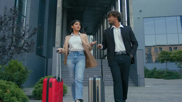 Two formal people walking at city outdoors outside airport arriving business trip talking together walk with luggage baggage talk cooperation partnership travel Indian Arabian colleagues man woman