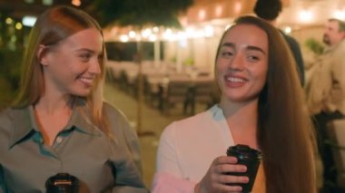 İki beyaz kadın ellerinde kahve fincanıyla şehir merkezinde yürüyorlar muhabbet ediyorlar gülüşüyorlar kafe dinlenme haftasonu eğlencesine eğleniyorlar pozitif ruh hali.