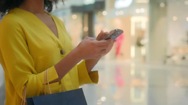 购物中心的女性使用智能手机手机小玩艺儿触摸陈列女孩包装购物者在商店技术内现代周末数字互联网在线流行 — 图库视频影像