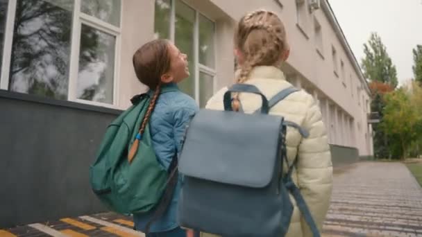 バックビュー2人の少女ガールフレンドは 友情を散歩する外の街を歩きます 学習者 女子姉妹 トータルネスチャット ユーモラスな遊び心のある子供たち 喜びを楽しみます 面白い動き — ストック動画