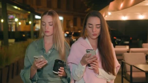 两个欧洲不快乐的女人走在夜市咖啡手机智能手机发短信和姐妹们聊天 朋友们忙得不可开交的女孩技术外面的小玩意卡住了电话都市社交媒体 — 图库视频影像