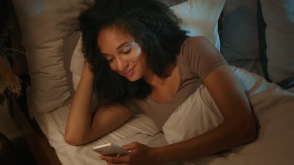 在床上躺在枕头上的非洲裔美国女人失眠在睡前浏览智能手机社交媒体在家里卧室里翻动手机应用程序 — 图库视频影像