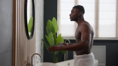 Gülümseyen Afro-Amerikan bir adam koltuk altına deodorant sürüyor. Her gün banyo aynasında aynaya bakıyor. Hijyen bozukluğu tedavisi görüyor.