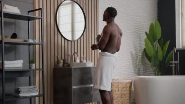 Komik, mutlu, Afro-Amerikan erkek, banyoda havluyla dans eden, aktif dans eden, ayna yansımasını gösteren, şarkı söyleyen, banyo sabah hijyeninde dinlenen, neşeli, tasasız erkek.