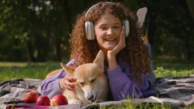 Beyaz, mutlu, kıvırcık saçlı kız. Kulaklıkla müzik dinliyor. Yaz pikniğinde dinleniyor.
