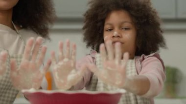 Mutlu Afro-Amerikan aile etnik annesi ve küçük kızı birlikte yemek yapmayı seviyorlar. Ev mutfağında kirli avuç içi un tozu, fırın keki, pasta pişirme, el yapımı eğlenceli anne ve çocuk kızı.