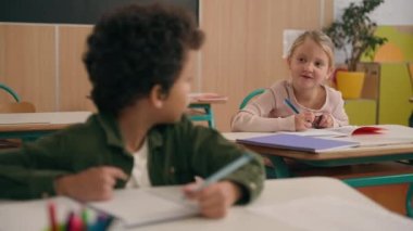 Çok ırklı küçük sınıf arkadaşları. Çok ırklı öğrenciler. İki çocuk. Kafkasyalı kız, Afrikalı Amerikalı erkeğin sınav yazma sınavına doğru cevap vermesini öneriyor.