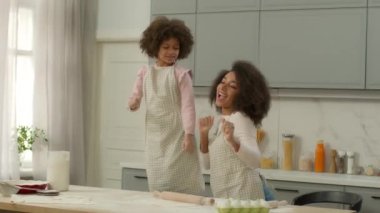 Mutlu Afro-Amerikan anne ve küçük kızı birlikte yemek pişiriyorlar hamur unu pişiriyorlar yemek pişiriyorlar anne ve çocuk bebek kız dans ediyorlar müzik ev partileri mutfağında dans ediyorlar