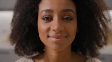 Güzel Afro-Amerikan kız gülümsüyor mutlu etnik kadın pozitif neşe dolu kadın evde gülümsüyor dişlek kameraya bakıyor oldukça sağlıklı kız arkadaş içeride kıvırcık saçlı portre ile.