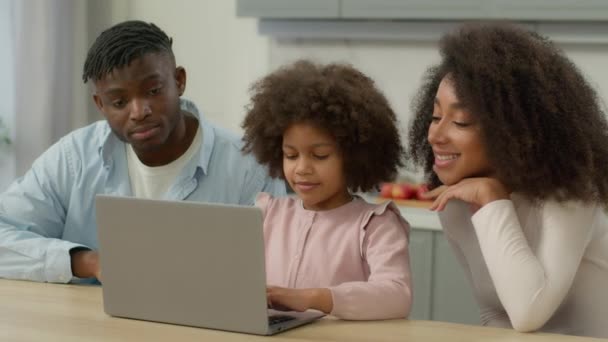 ハッピー アフリカ系アメリカ人家族 母親と小さな子供のエスニック 母親の父親 子供の娘 家庭のキッチンでラップトップのタイピング コンピュータを使用して学ぶ ペアレンタル コントロール — ストック動画