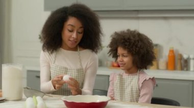 Mutlu bir aile, mutfakta birlikte yemek pişiriyor. Afro-Amerikan anne, küçük kızına kek hamurunu birlikte pişirmesini öğretiyor. Anne, yumurta sütü karışımı elek tarifini gösteriyor.