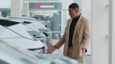 Şaşırtıcı etnik adam, Afro-Amerikalı erkek iş adamı gülümseyen alıcı galeride yeni elektrikli lüks araba modelinin bagajına bakıyor mutlu müşteri galeride araba satışı hayali kuruyor.