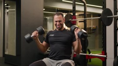 Latin kökenli çok ırklı Amerikalı güçlü bir adam spor salonunda oturuyor halterleri kaldırıyor ağır metal ekipmanları çalıştırıyor omuz ağrısı çekiyor erkek sporcu vücut geliştirme sporu sakatlığı