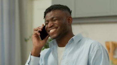 Mutlu Afrikalı Amerikalı çift ırklı erkek, gülümseyen, konuşan, cep telefonlu, arkadaşlarıyla konuşan, gülen, neşeli, neşeli, neşeli, mutlu, akıllı telefon konuşmalarını evde tartışan etnik bir adam.