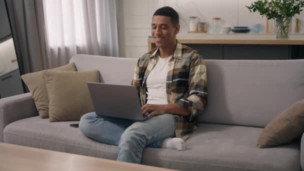 笑顔のアフリカ系アメリカ人男性 ソファの家賃ローンユーザーフリーランサー 学生ビジネスマン Pcラップトップコンピュータ オンラインショッピング 有料ブラウジングを使用してソファーアパートでリラックス — ストック動画