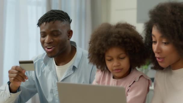 快乐的家庭非洲裔美国人妈妈爸爸和小女儿一起在家里的厨房里网上购物笔记本电脑信用卡笑着妈妈爸爸小女孩买定购单 — 图库视频影像