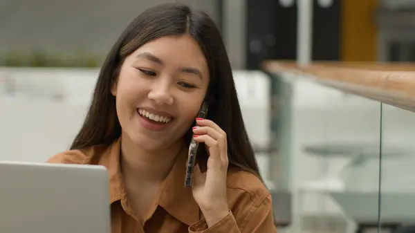 オフィスでラップトップでオンラインで働くアジアの女性ビジネス女性を笑顔中国の女子学生フリーランスの話携帯電話笑い興奮した女性の答えスマートフォン呼び出し屈託のない会話 — ストック写真