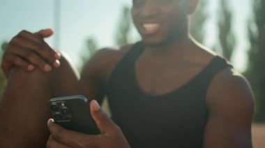Afrikalı Amerikalı gülümseyen sporcu hippi elinde akıllı telefon sosyal medya tebessümü neşeli, rahat sporcu erkek futbolcu cep telefonuyla şehirde antreman yaptıktan sonra rahatla.